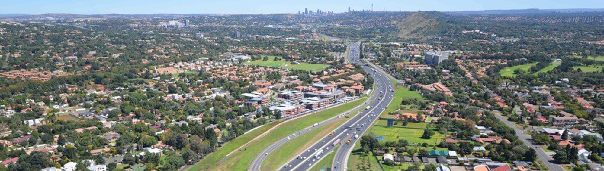 Aerial view of Ekurhuleni showcasing residential areas alongside the highway with Johannesburg skyline in the distance.