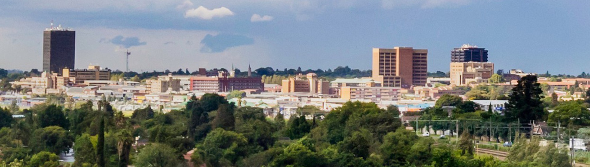 Panoramic view of Kempton Park with urban buildings surrounded by lush greenery under a cloudy sky.
